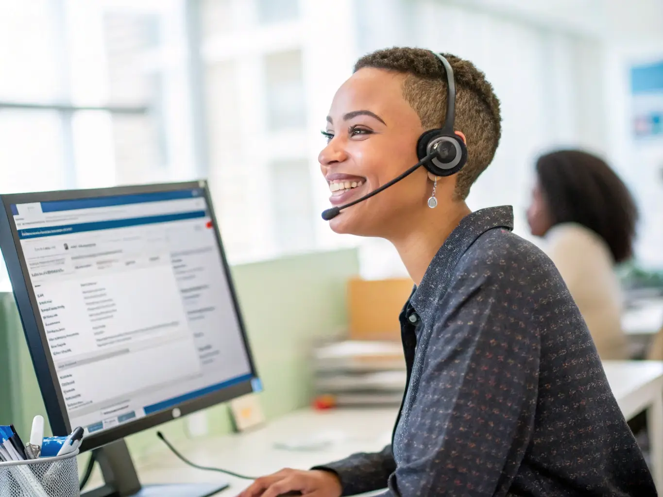 An image of a support agent wearing a headset, assisting a client via computer.